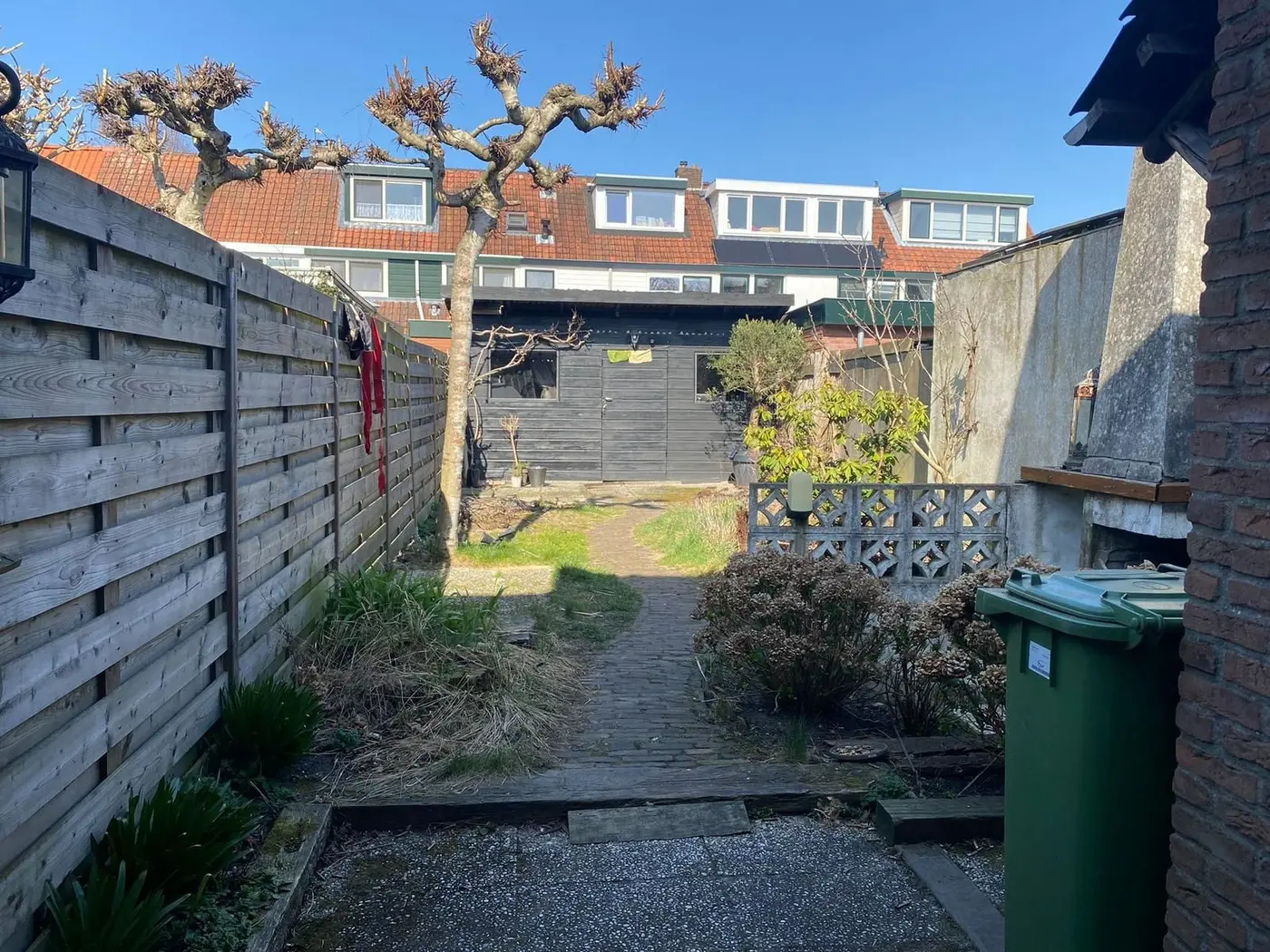 De achtertuin voor de renovatie: verweerde schutting, kale grond en een oude schuur