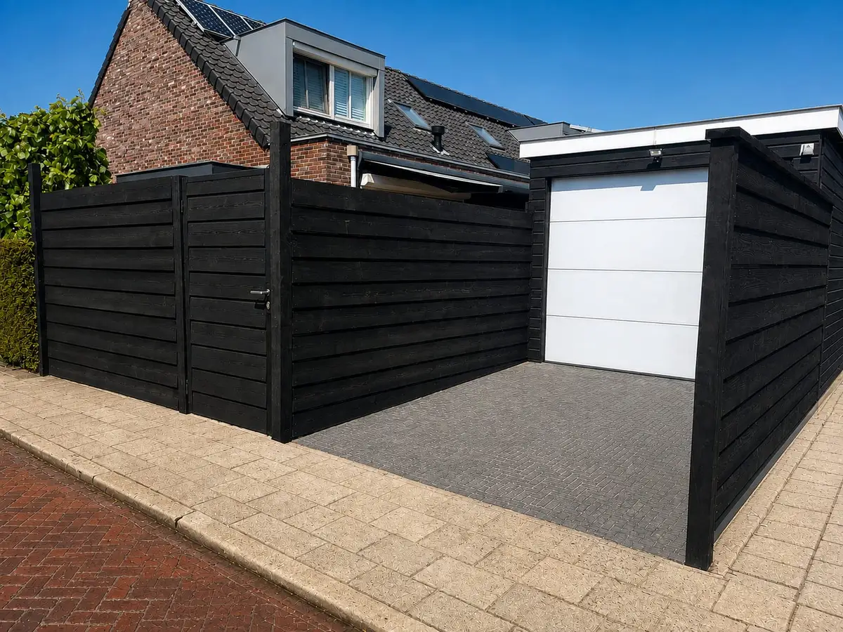 Afgebouwde zwarte houten schutting met een poort, rondom een oprit naast een garage